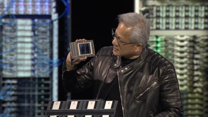 Ένα άτομο με μαύρο δερμάτινο μπουφάν κρατά ένα τσιπ υπολογιστή στο χέρι του ενώ στέκεται μπροστά σε ένα φόντο με θέμα την τεχνολογία.