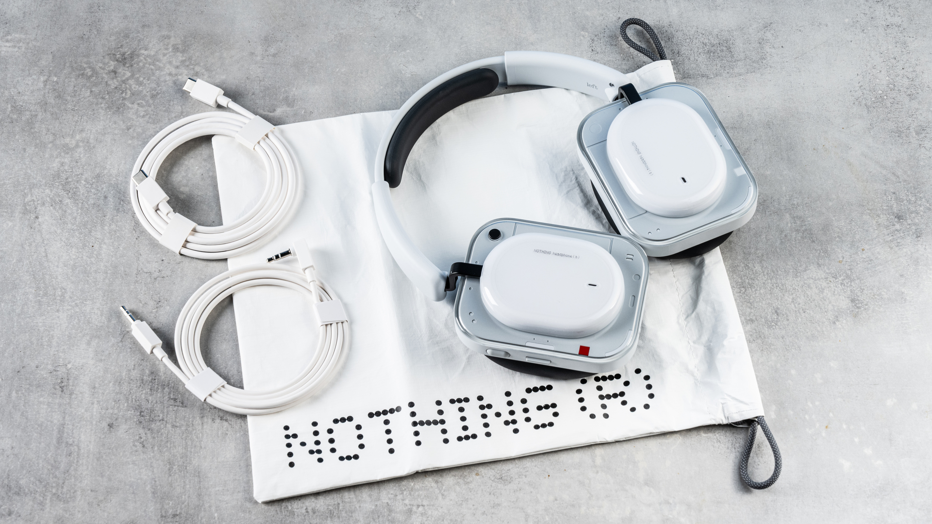 the nothing headphone (a) photographed against the blue tom's guide background, showing the transparent and white ear cups with red accents, the padded headband, and the accessories including 3.5mm jack
