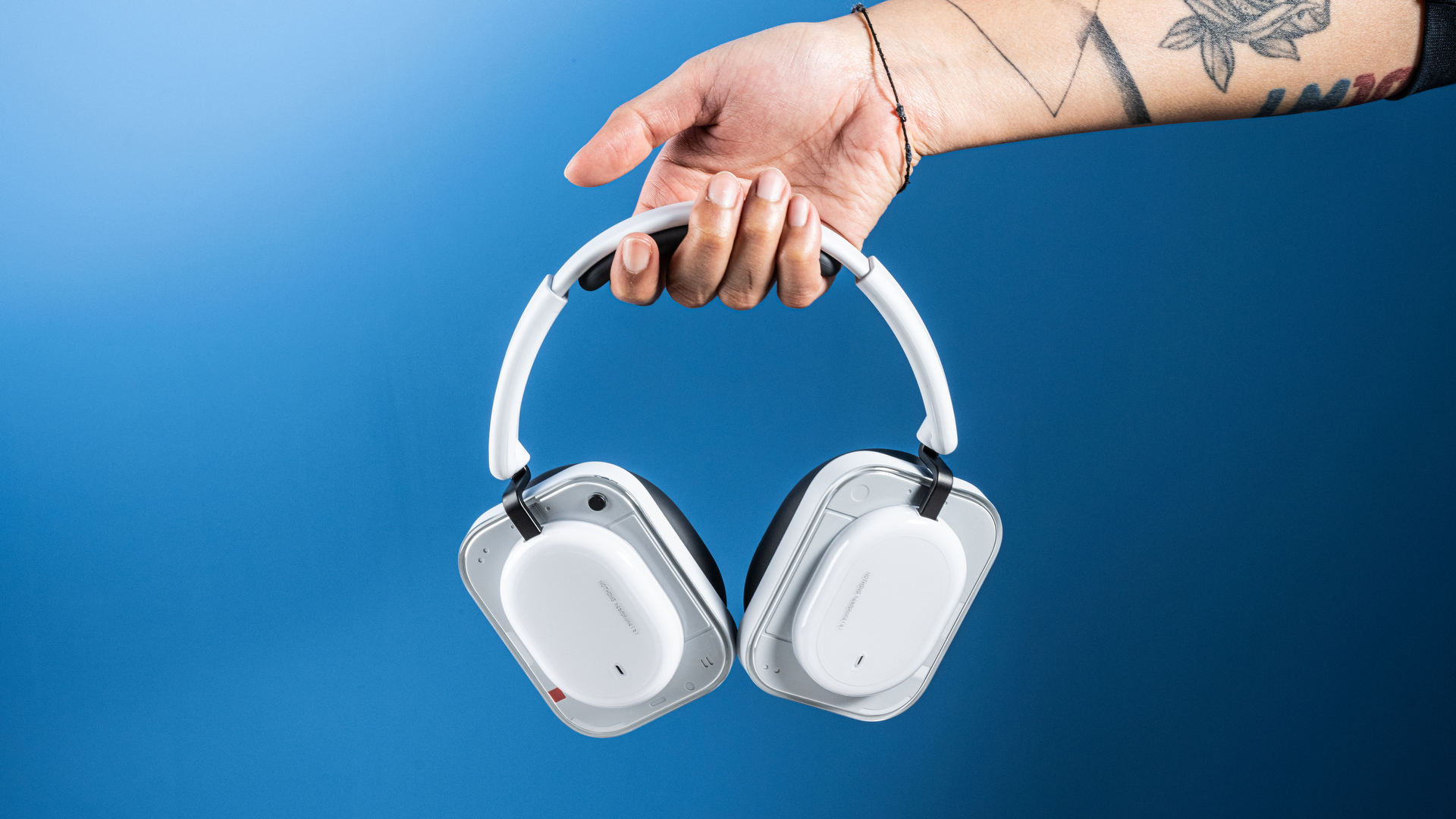 the nothing headphone (a) photographed against the blue tom's guide background, showing the transparent and white ear cups with red accents, the padded headband, and the accessories including 3.5mm jack