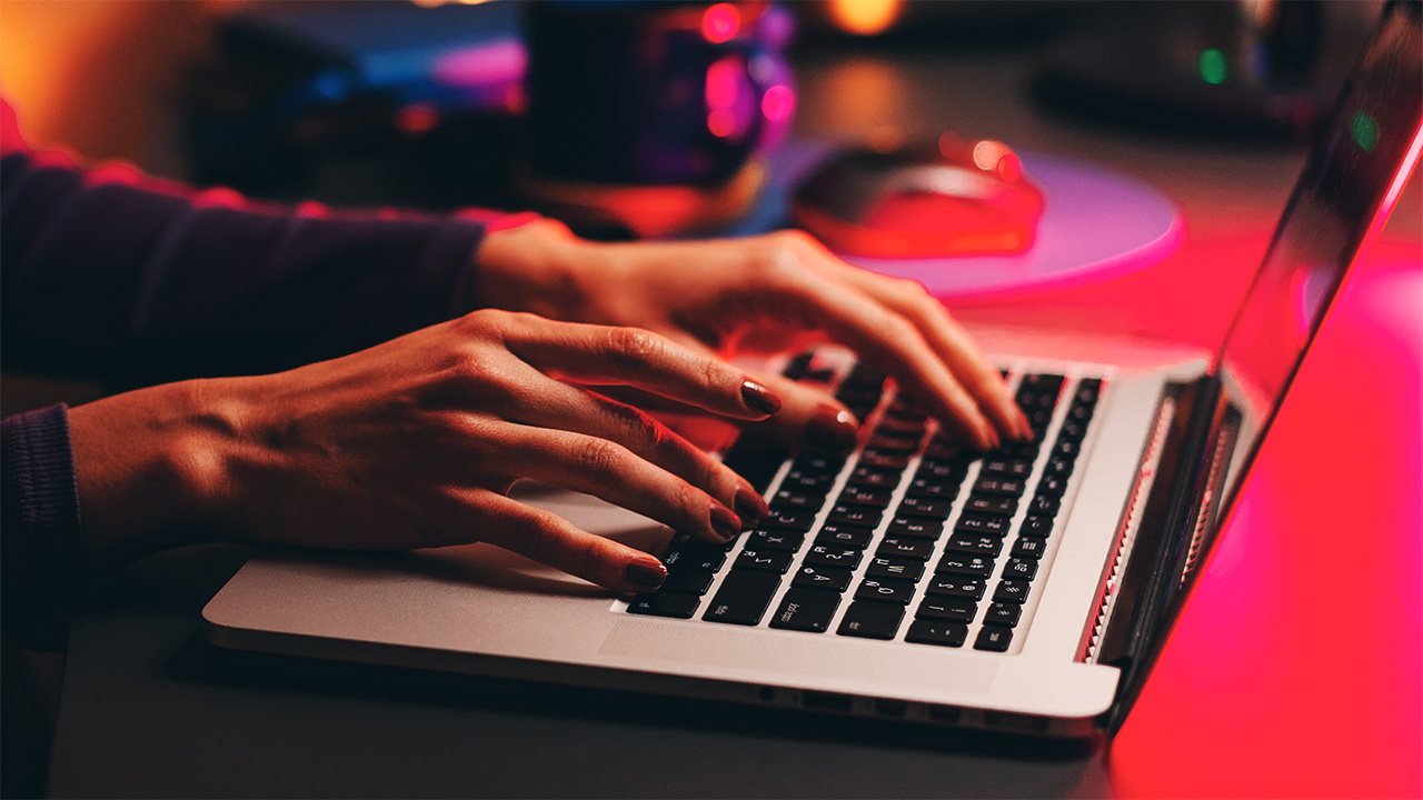 Άτομο που πληκτρολογεί σε φορητό υπολογιστή σε δωμάτιο με χαμηλό φωτισμό