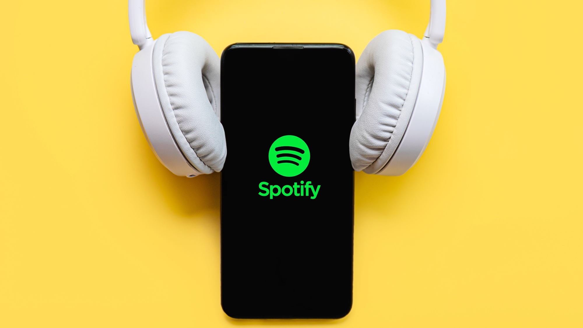 Λογότυπο Spotify σε τηλέφωνο με λευκά ακουστικά που στηρίζονται στο τηλέφωνο