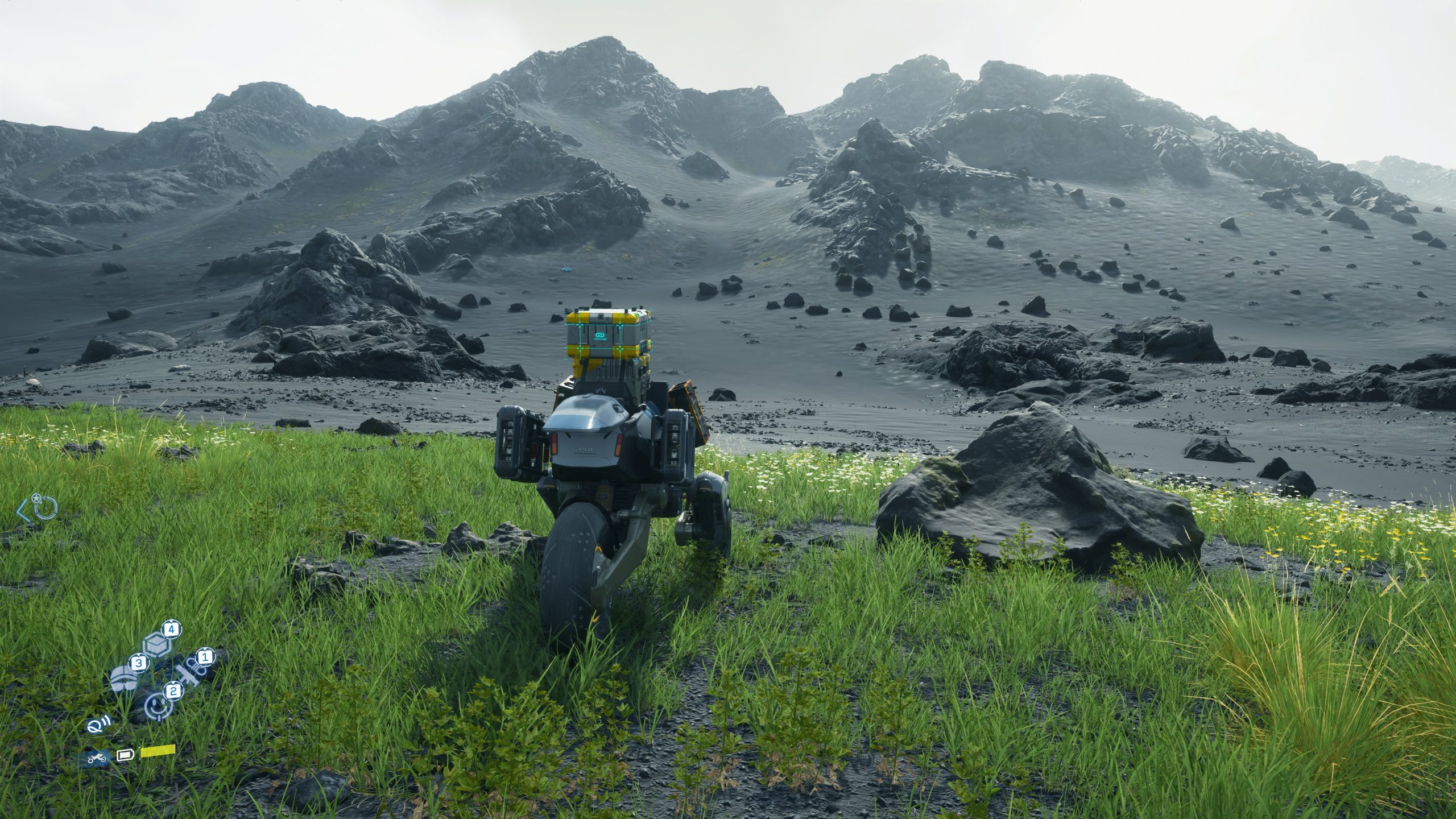 A character in Death Stranding riding a motorcycle across a grassy plain towards a rocky mountain.