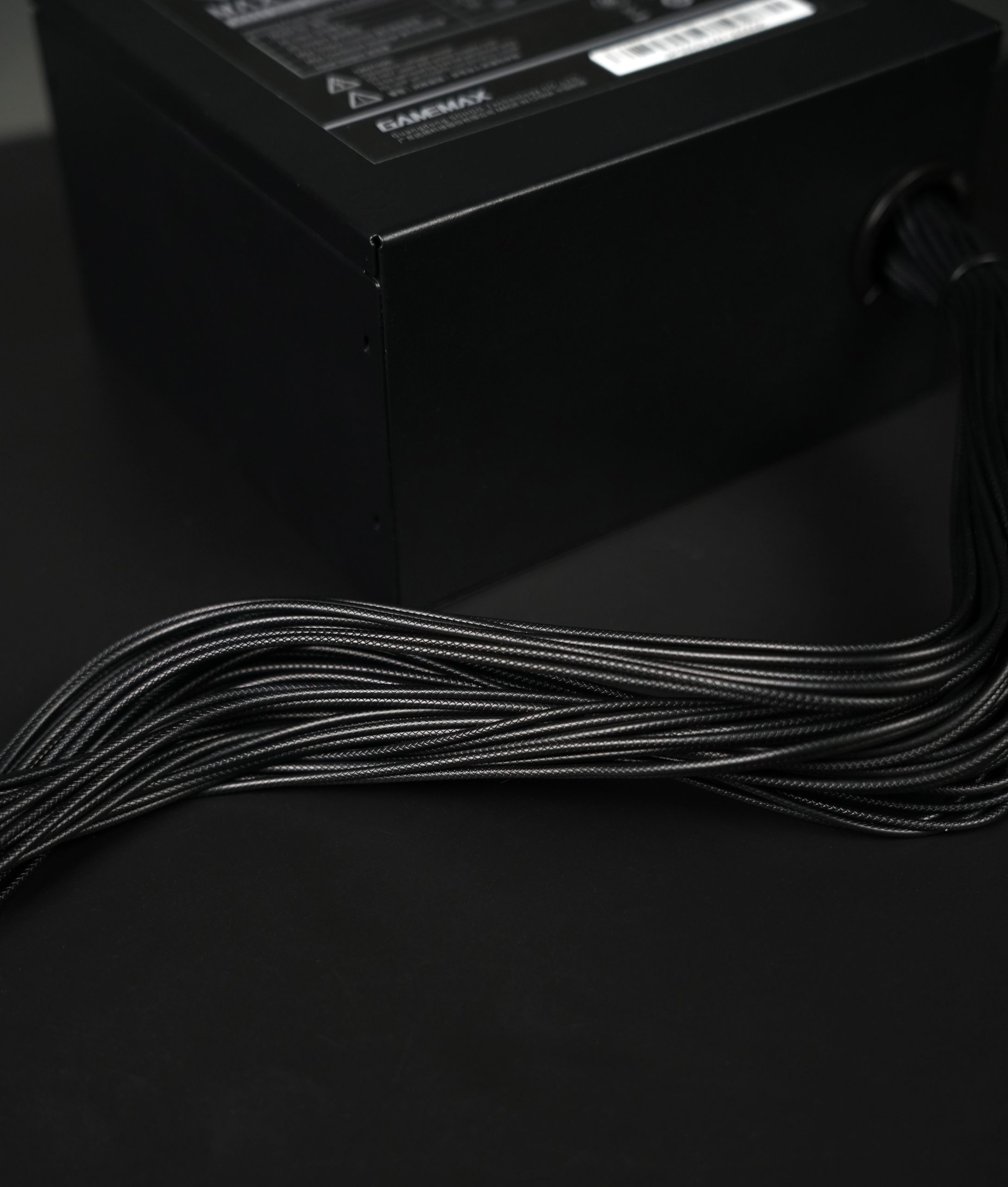 Μια μαύρη μονάδα τροφοδοσίας GameMax με πολλαπλά πλεγμένα καλώδια που εκτείνονται από αυτήν.