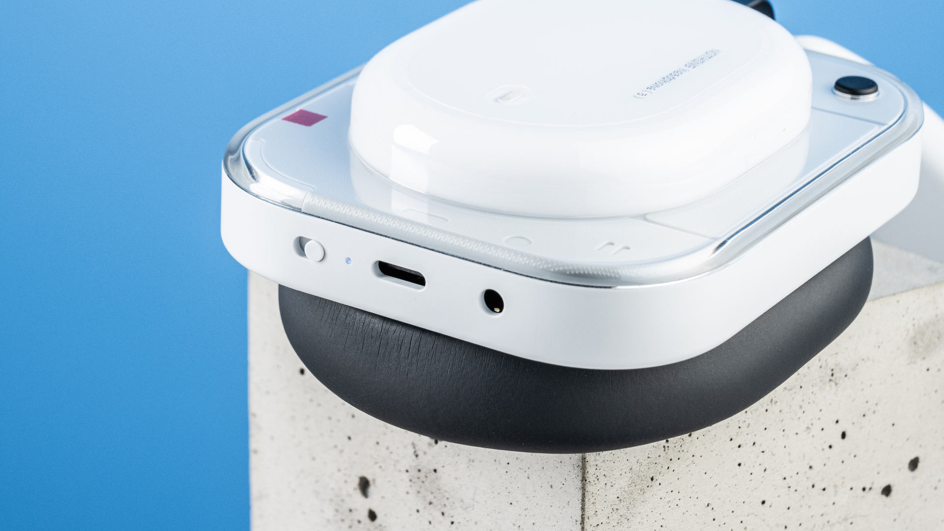 the nothing headphone (a) photographed against the blue tom's guide background, showing the transparent and white ear cups with red accents, the padded headband, and the accessories including 3.5mm jack