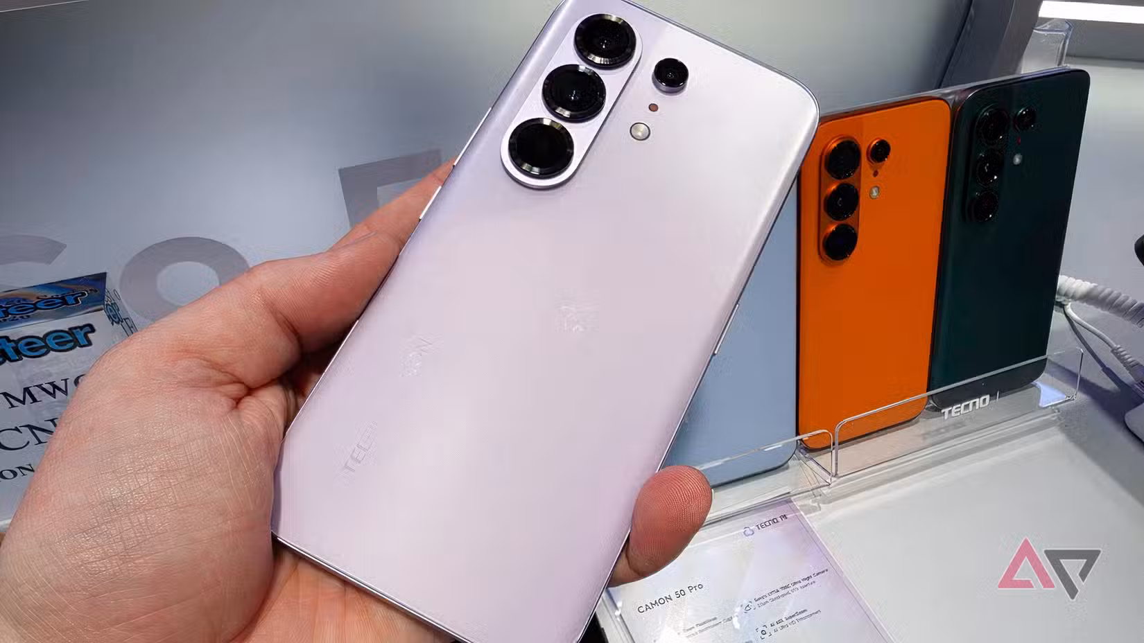 Το Tecno Camon 50 Pro στο ανδρικό χέρι, μπροστά από πολλά άλλα μοντέλα του τηλεφώνου.