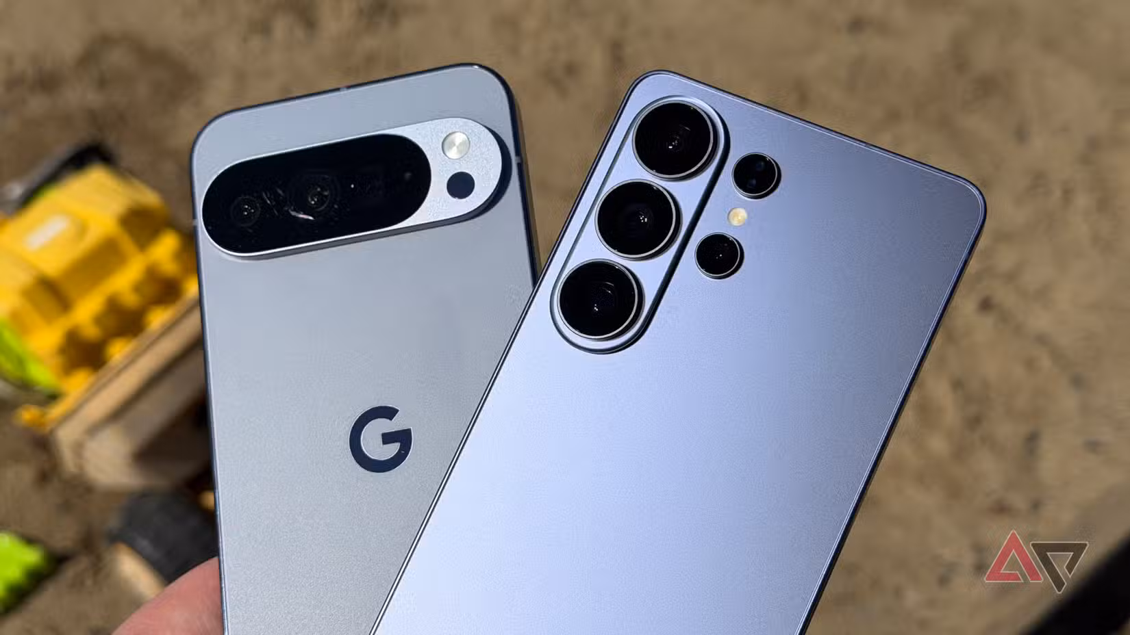 Τα Galaxy S26 Ultra και Pixel 10 Pro XL κρατούνται μια ηλιόλουστη μέρα πάνω από ένα sandbox