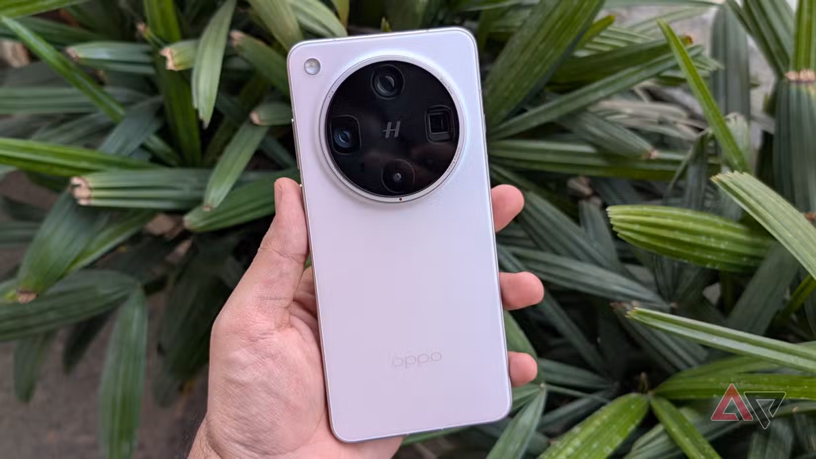 Pink Oppo Find X8 Ultra Android smartphone στο χέρι μπροστά από πράσινα φύλλα