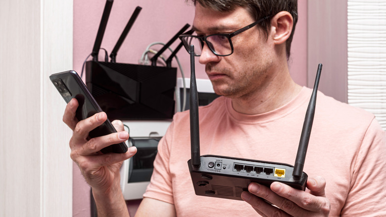 Άτομο που κρατά έναν ασύρματο δρομολογητή στο ένα χέρι και μια κινητή συσκευή στο άλλο.